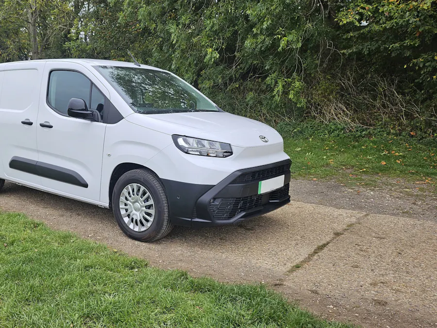 Clean white work van parked on a gravel track beside a hedge